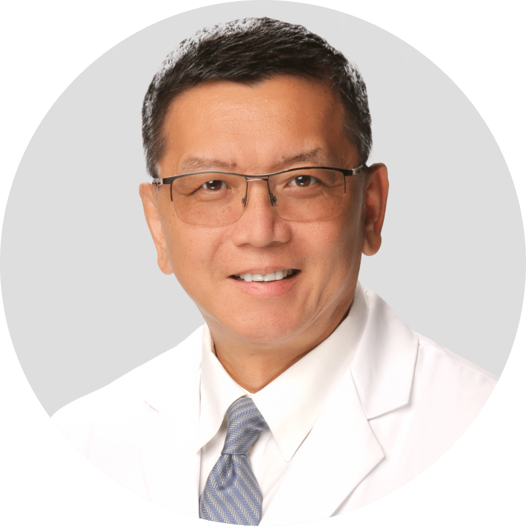 Man wearing glasses, a white coat, and a light blue tie, smiling at the camera against a plain background.