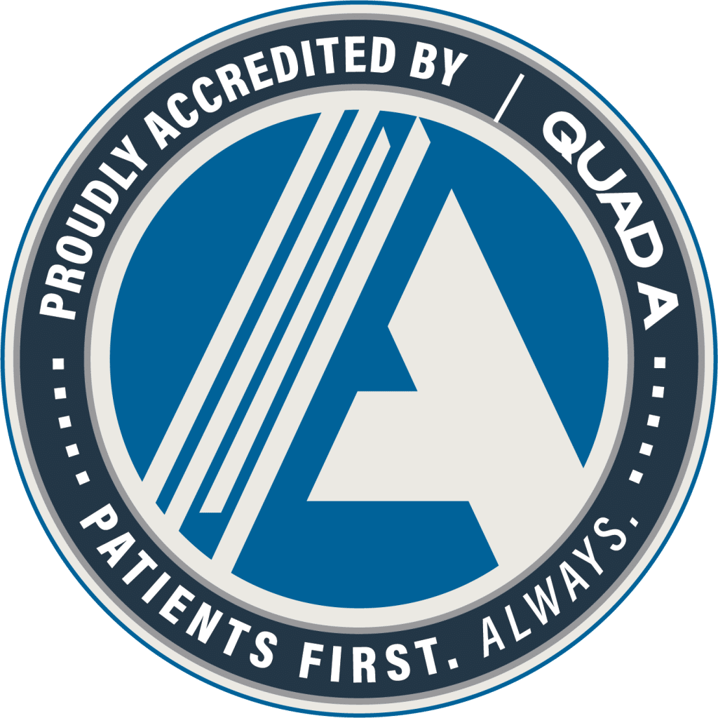Circular badge with the text "Proudly Accredited by QUAD A. Patients First. Always." surrounding a stylized letter "A" logo in blue and white.