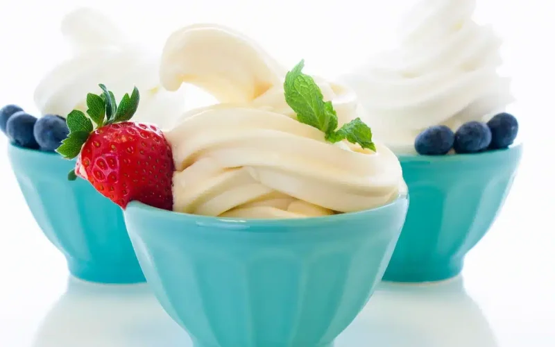 Three blue bowls of vanilla frozen yogurt, each garnished with blueberries; the front bowl has a strawberry and mint leaves as additional garnish.