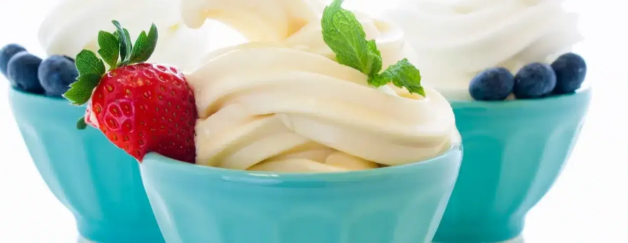 Three blue bowls of vanilla frozen yogurt, each garnished with blueberries; the front bowl has a strawberry and mint leaves as additional garnish.