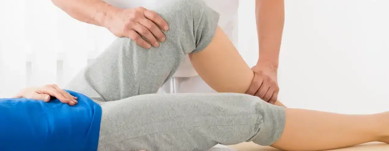 A physical therapist assists a person lying on a table by bending their knee and hip during a rehabilitation or therapy session.