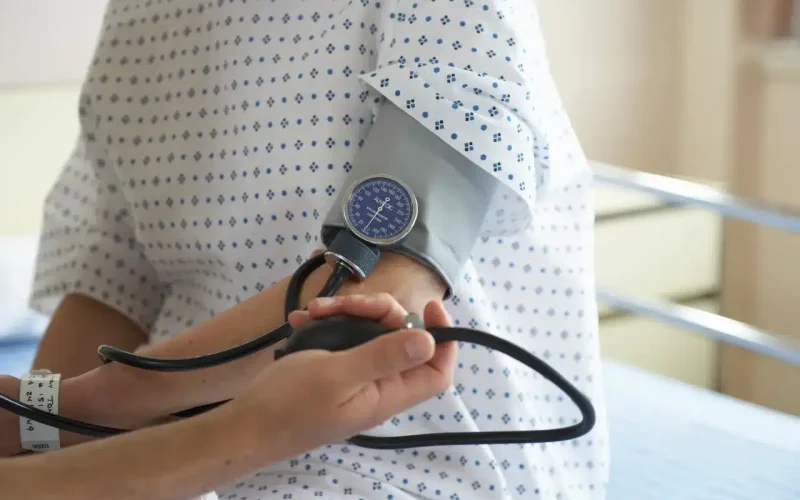 A person in a hospital gown is having their blood pressure measured with a manual sphygmomanometer by a healthcare worker.