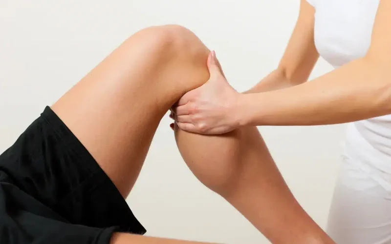 A person lying down receives a knee and calf massage or physical therapy from another person.
