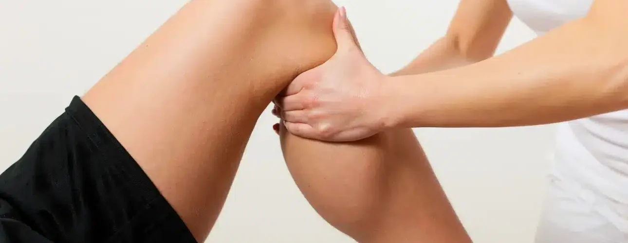 A person lying down receives a knee and calf massage or physical therapy from another person.