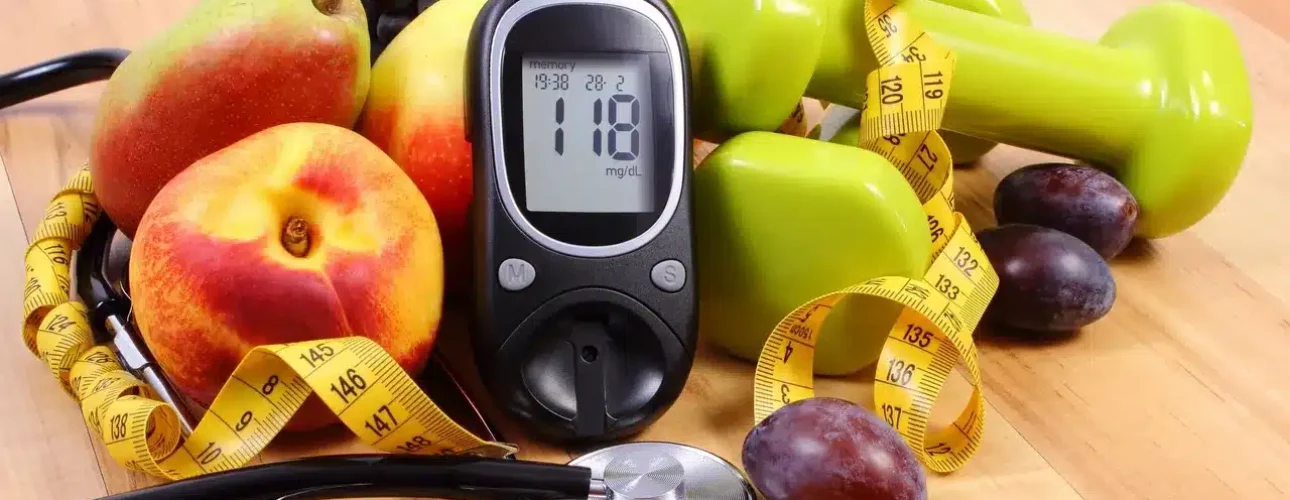 A blood glucose meter shows 118 mg/dL, surrounded by fruits, green dumbbells, a tape measure, and a stethoscope on a wooden surface.