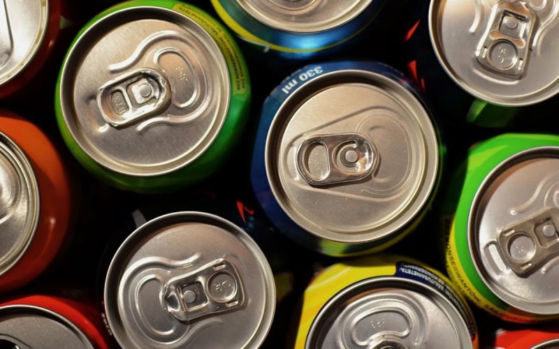 Close-up of the tops of several aluminum soda cans in various colors, showing pull tabs and parts of the can labels.