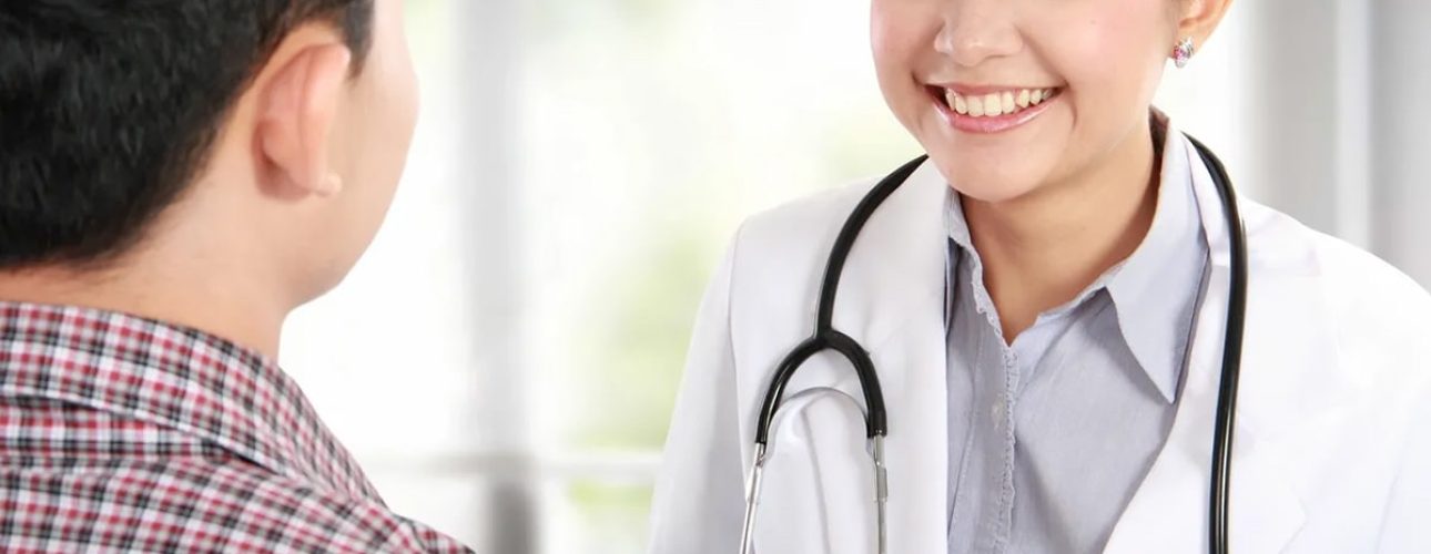 A doctor with a stethoscope smiles and speaks to a patient wearing a plaid shirt during a medical consultation.