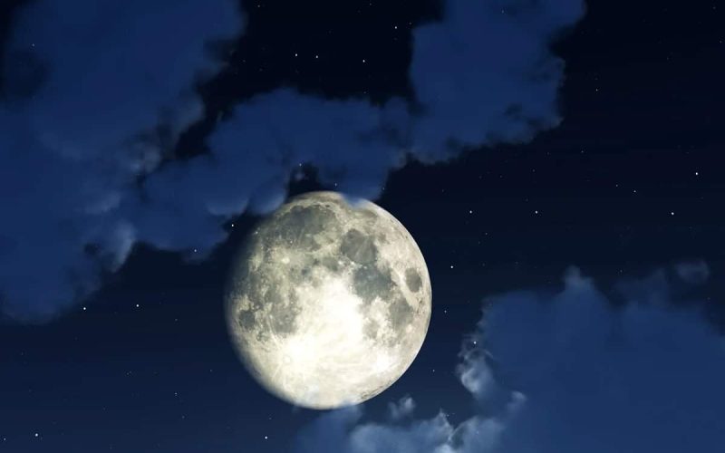 A bright full moon shines in a dark night sky, surrounded by scattered clouds and faint stars.